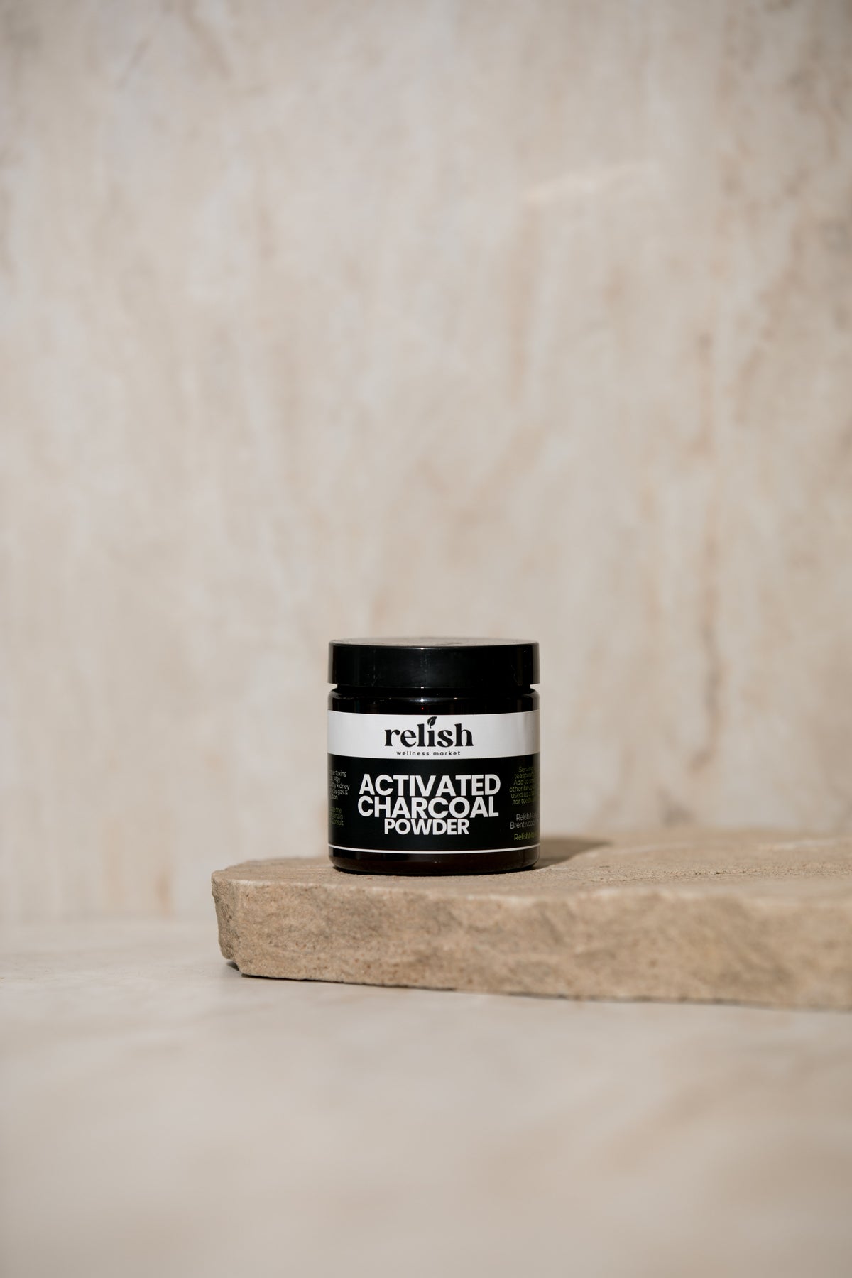 Jar of Relish Market activated charcoal powder on a wooden block with a beige background