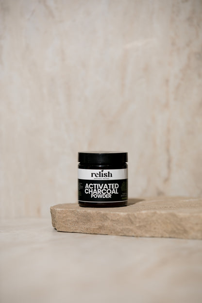 Jar of Relish Market activated charcoal powder on a wooden block with a beige background