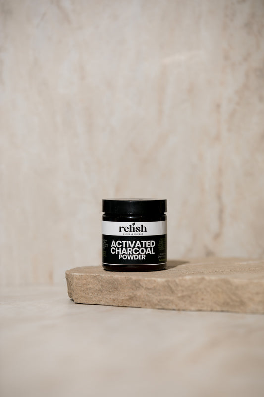 Jar of Relish Market activated charcoal powder on a wooden block with a beige background