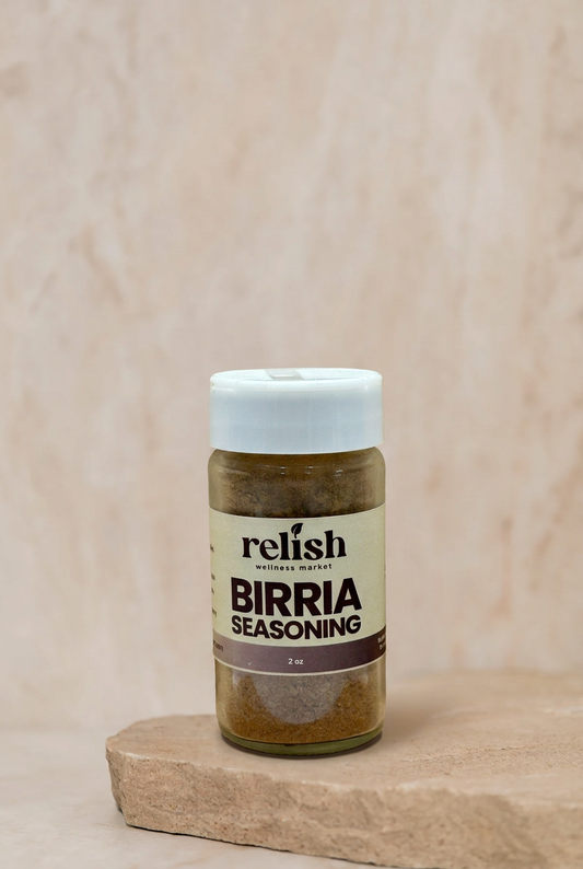 A bottle of Relish Market Birria Seasoning with a white cap and cream label, displayed on a rustic wooden block against a textured beige background.