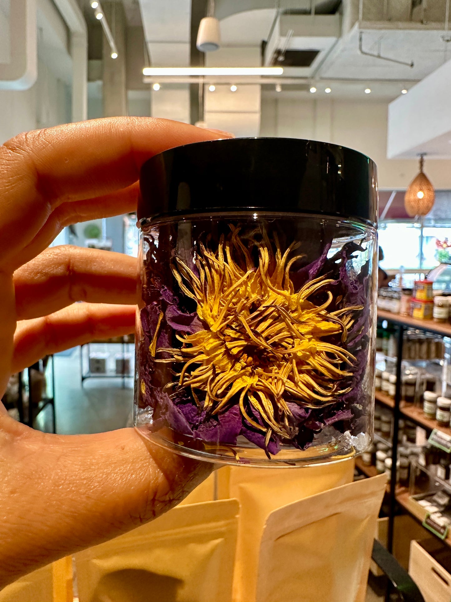 Hand holding jar of blue lotus flowers by Relish Market - with a wellness store view as a background.