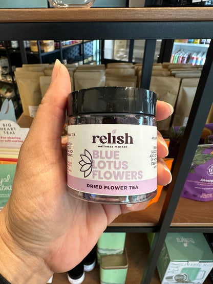 hand holding a jar of Blue Lotus Flowers by Relish Market - against the background of store shelves.