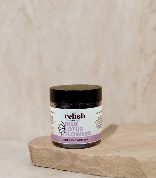 A small jar of Relish Market Blue Lotus Flowers dried flower tea sits on a textured stone slab against a neutral beige marble background.