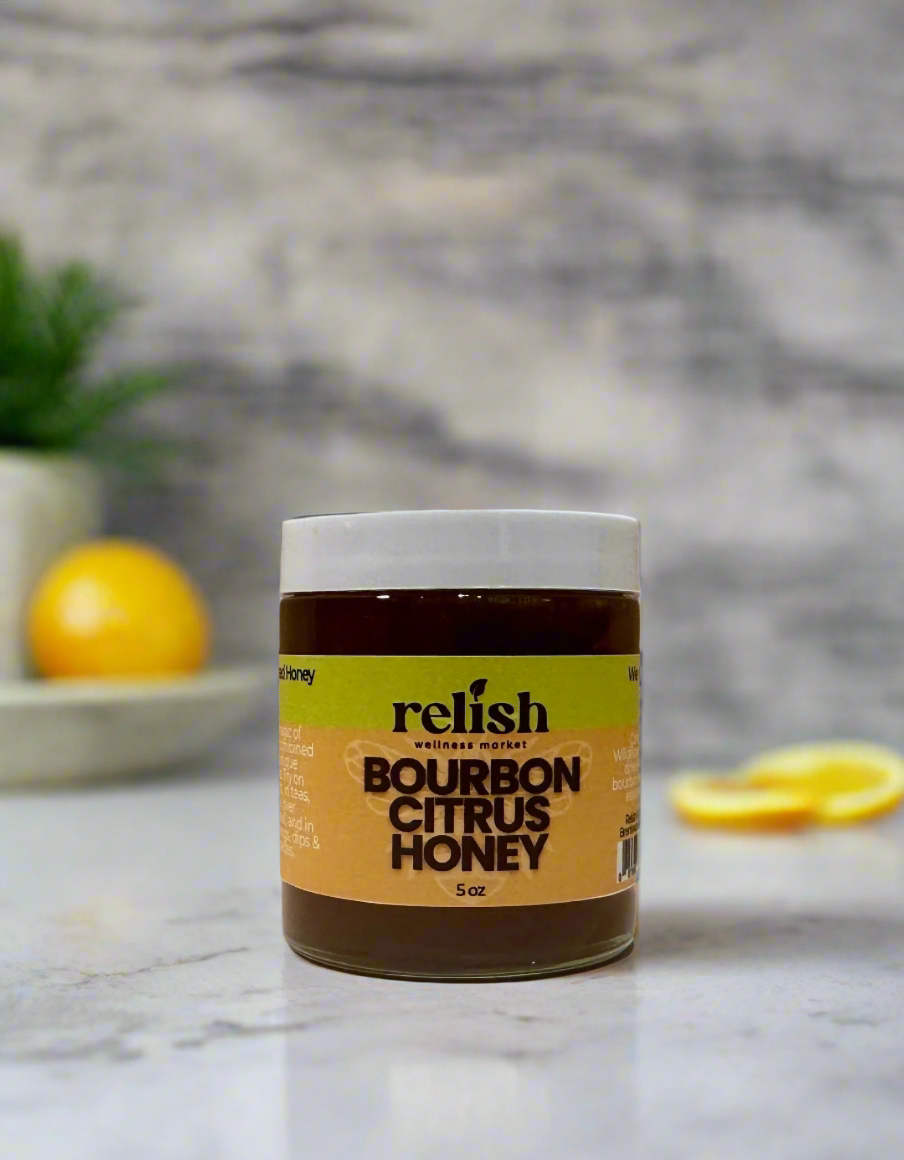 A jar of Bourbon Citrus Honey by Relish Market on a marble background with lemons.
