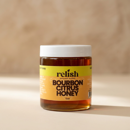 Close-up of a jar of Bourbon Citrus Honey  by Relish Market. Raw unfiltered honey infused with bourbon and citrus.