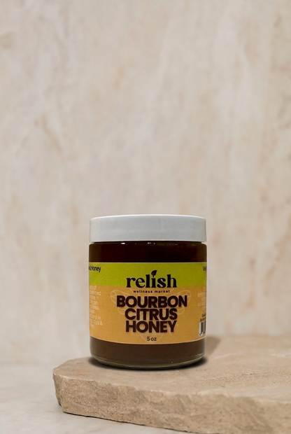 A jar of Bourbon Citrus Honey on a stone slab and neutral background. All natural Infused honey.