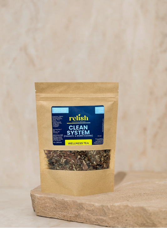 A stand-up kraft paper pouch of Relish Market Clean System Wellness Tea with a clear window showing loose tea leaves, set on a stone slab against a textured beige background.