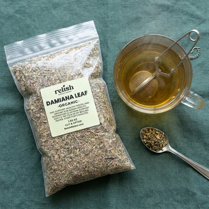 Damiana Leaf tea flat-lay on a green cloth with a glass mug of tea and a spoon full of damiana leaf.