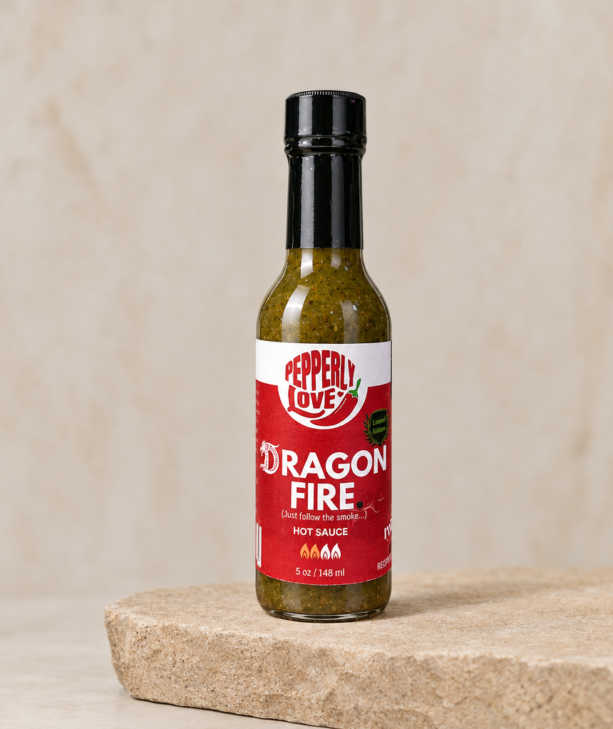 A bottle of Peppery Love Dragon Fire hot sauce standing on a stone slab against a textured beige background.