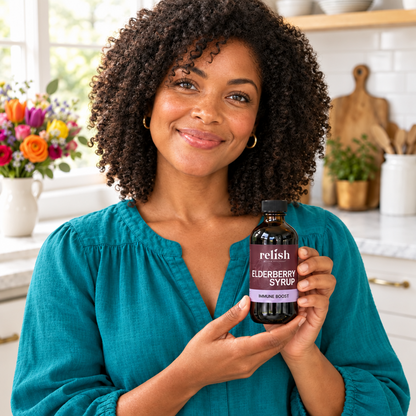 Woman in a colorful teal top holding Relish Market elderberry syrup in a brightly lit kitchen.