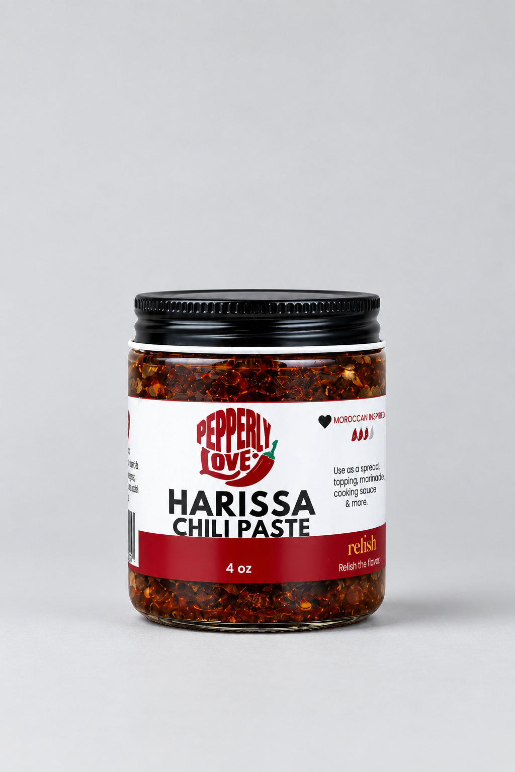 A 4 oz glass jar of Pepperly Love Harissa Chili Paste with a black metal lid, set against a clean light gray background.