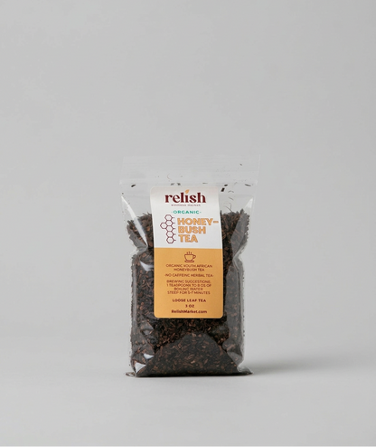 A clear stand-up pouch of Relish Market Organic Honey-Bush Tea on a light gray background. The packaging features a white and orange label, and the tea inside is visible through the transparent bag.