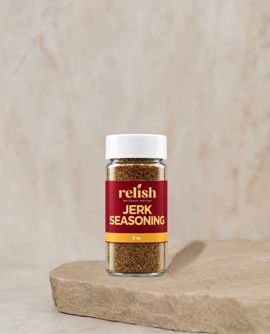 A glass jar of Jerk Seasoning Blend by Relish Market siting on a rock slab with a neutral beige background.