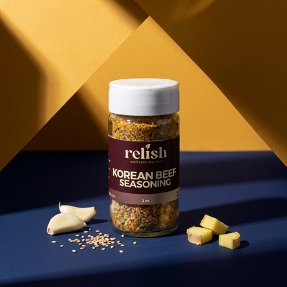 A jar of Korean Beef Seasoning by Relish Market with garlic cloves, sesame seeds and small pieces of cut ginger.