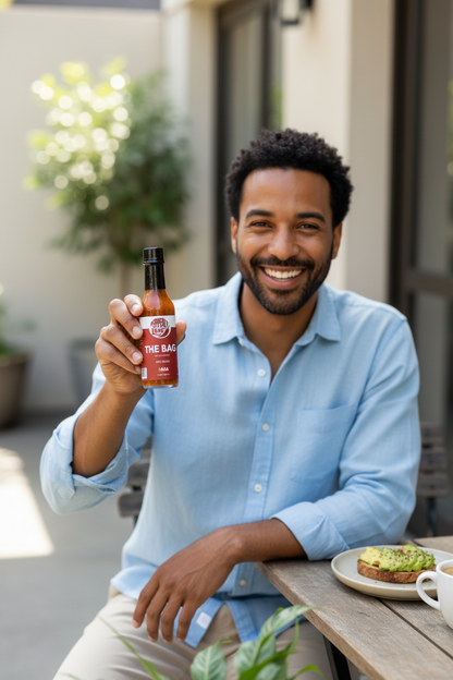 Man sitting outside at a table with food and holding a bottle of Pepperly Love Large The Bag Hot Sauce