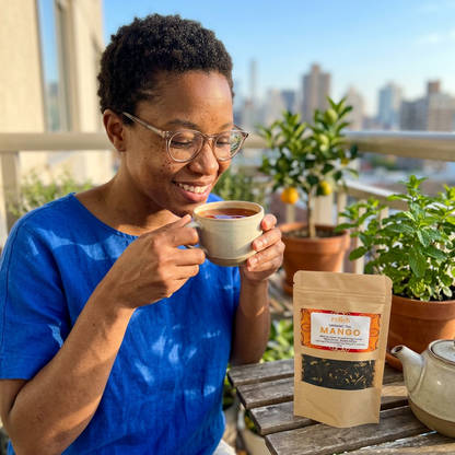 Woman enjoying a cup of Relish Market Mango Tea on a balcony with a city scene in the background.