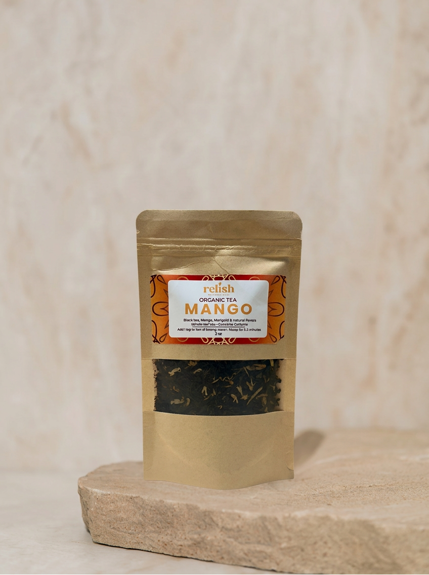 A stand-up pouch of Relish Market Organic Mango tea, displayed on a textured stone slab against a neutral beige marble background.