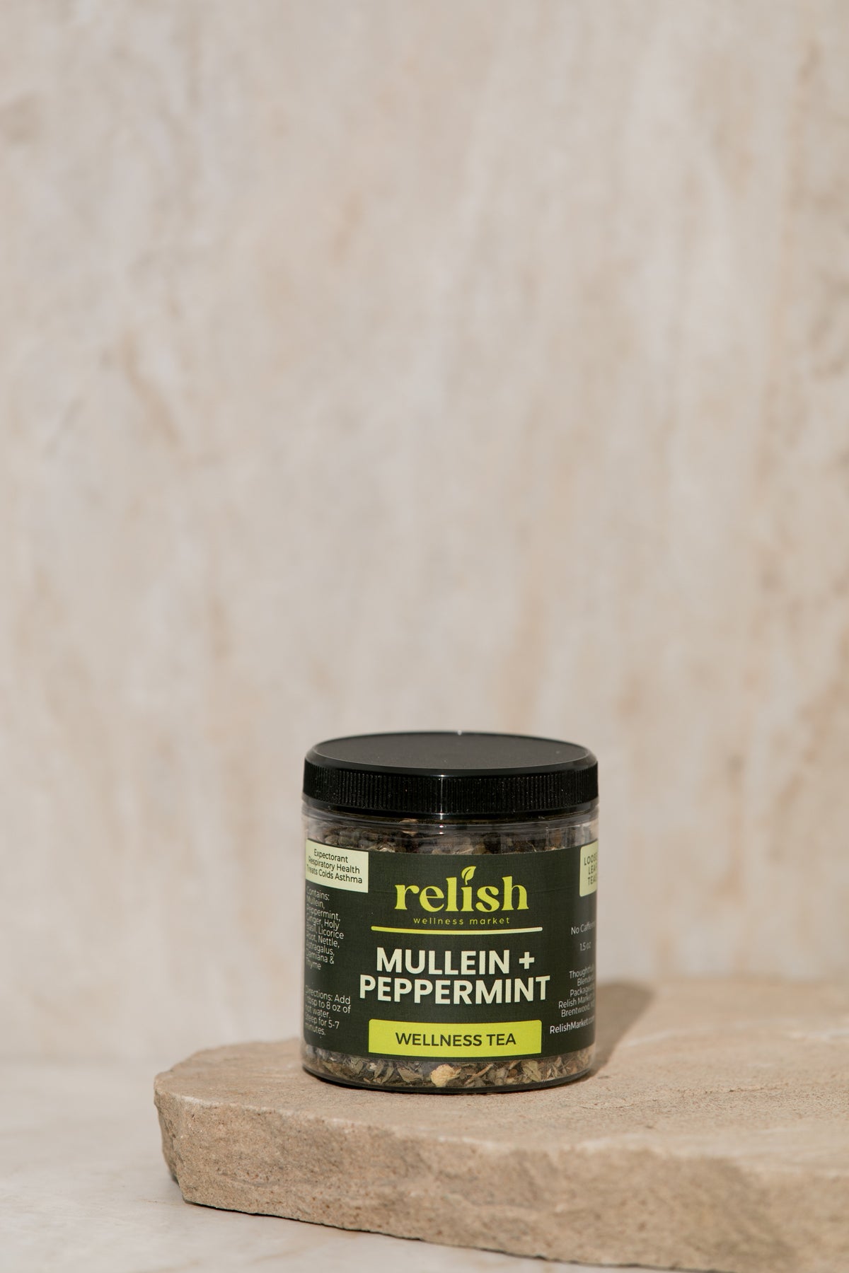 A jar of Mullein & Peppermint Wellness Tea by Relish Market, showing loose leaf tea mix inside a jar with a label and place on a stone slab