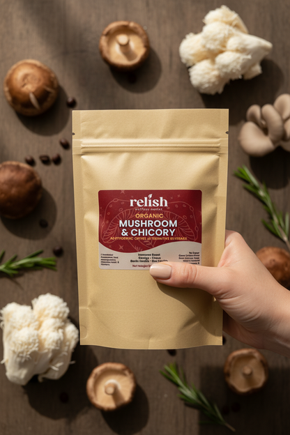 A hand holds a stand-up pouch of Relish Organic Mushroom & Chicory against a dark rustic background with mushrooms, cauliflower, rosemary, and coffee beans.
