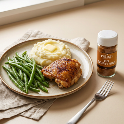 a jar of On Everything Spice Blend by Relish Market next to a beige plate of  chicken, string beans, and mashed potatoes.