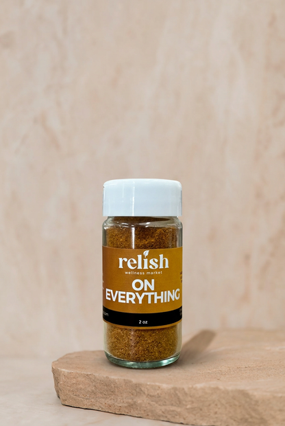 A 2 oz glass jar of 'Relish Market On Everything' seasoning blend, featuring a white cap and a brown label, displayed on a rustic stone slab against a textured beige background. A season-all for any dish