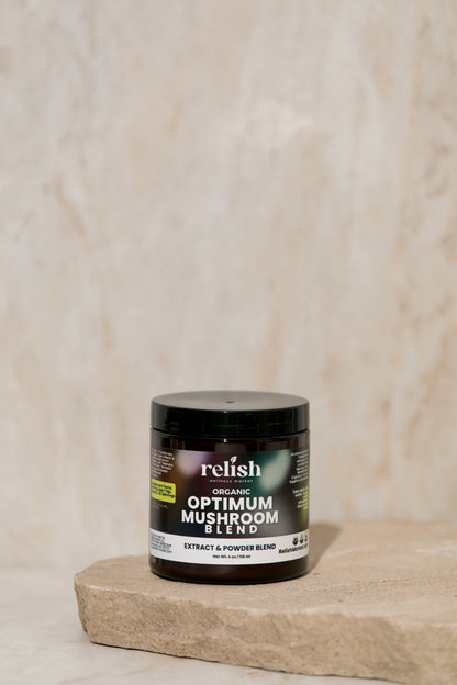 A jar of Optimum Mushroom Powder by Relish Market sits on a rustic stone slab set against a beige textured background.