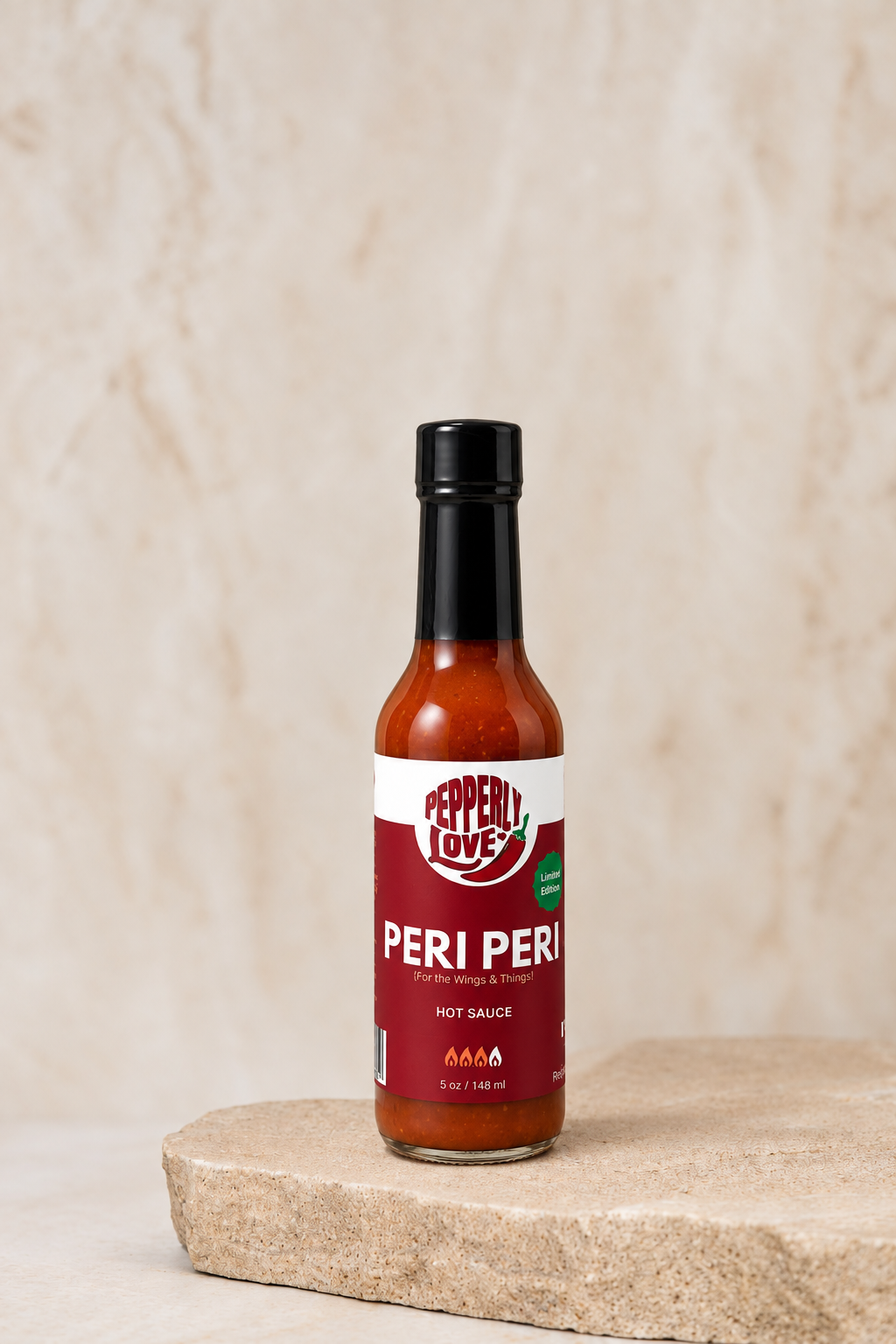 A bottle of Pepperly Love Peri Peri hot sauce stands on a light stone slab against a textured beige background.
