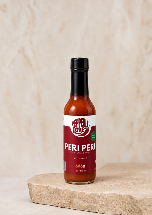 A bottle of Pepperly Love Peri Peri hot sauce stands on a light stone slab against a textured beige background.