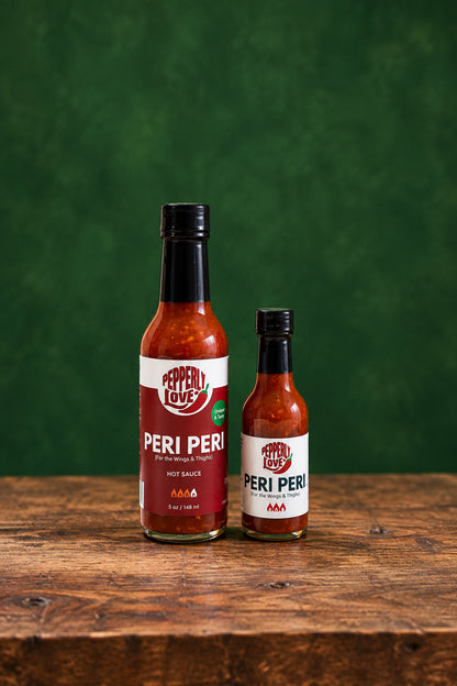Two bottles of Peri Peri sauce on a bold green background and wood tabletop
