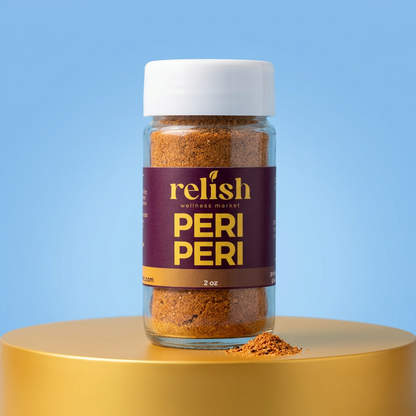 A 2 oz glass jar of Relish Wellness Market  Peri Peri seasoning, featuring a white lid and a dark purple label with gold lettering, displayed on a gold pedestal against a light blue background.