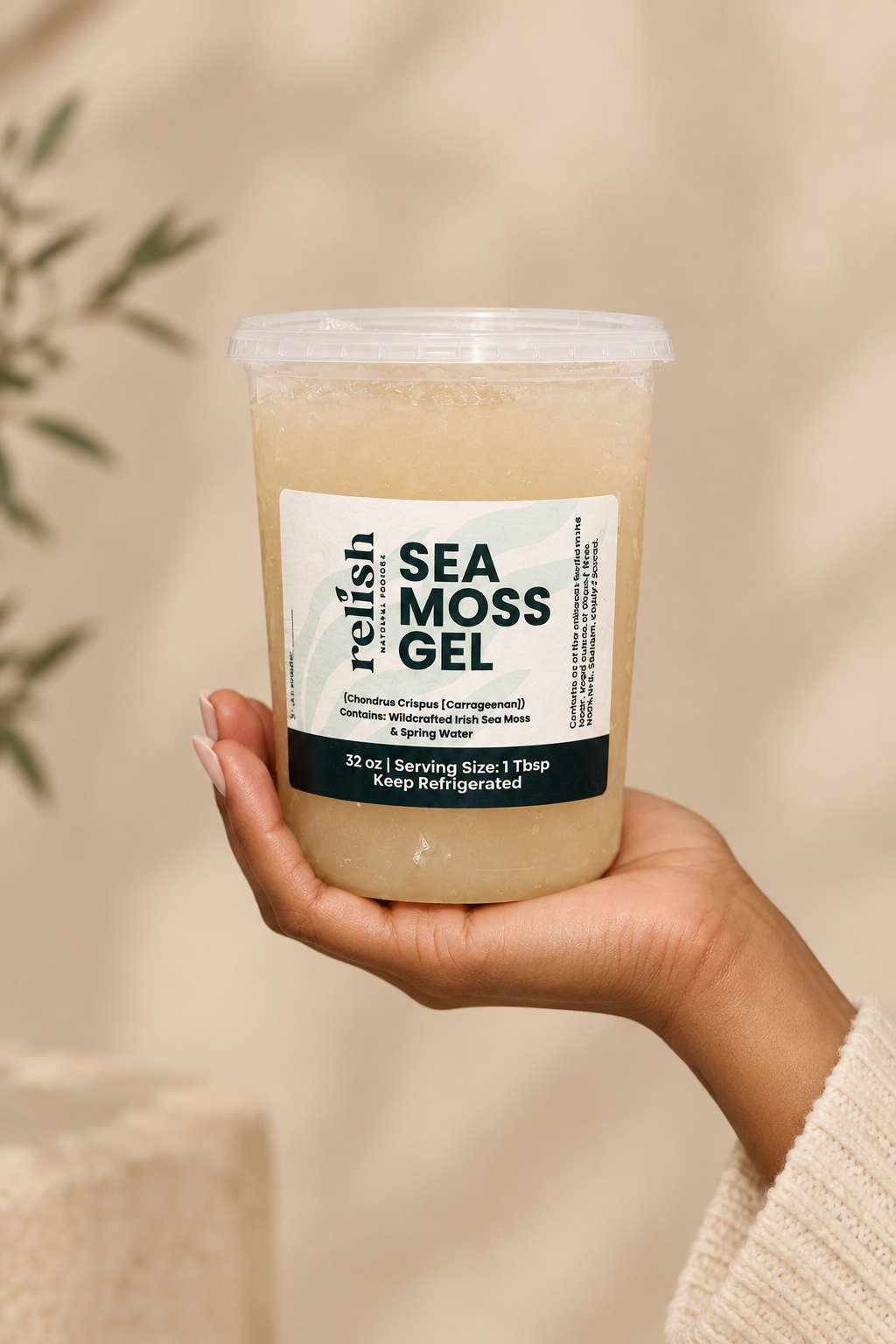 A hand holding a clear plastic tub of Relish Market's 32 ounce Sea Moss Gel against a warm beige background with soft leaf shadows.