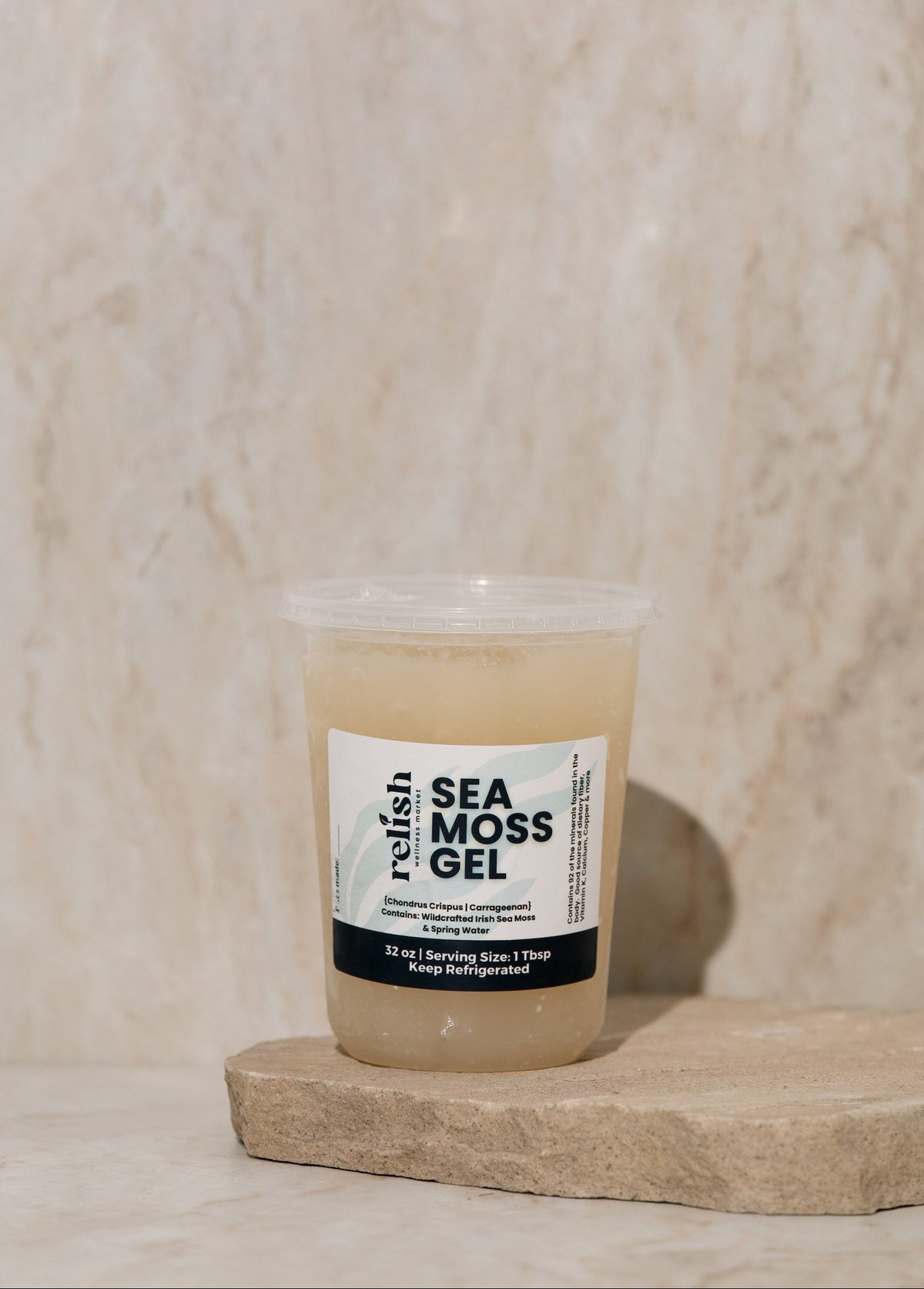 Clear container of Sea Moss Gel with a label on a wooden surface set against a beige textured background.