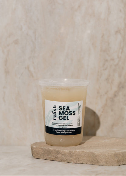 Clear container of Sea Moss Gel with a label on a wooden surface set against a beige textured background.