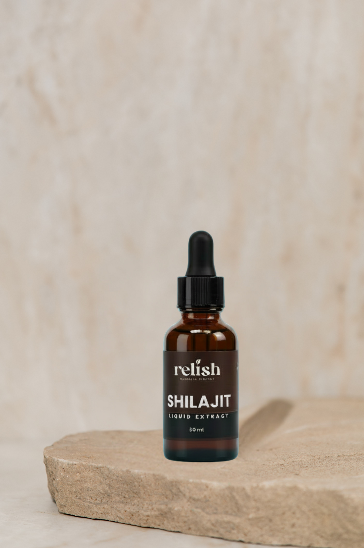 A 10ml amber glass dropper bottle of Relish Shilajit Hair Extract, standing on a rustic stone slab against a textured beige stone background.
