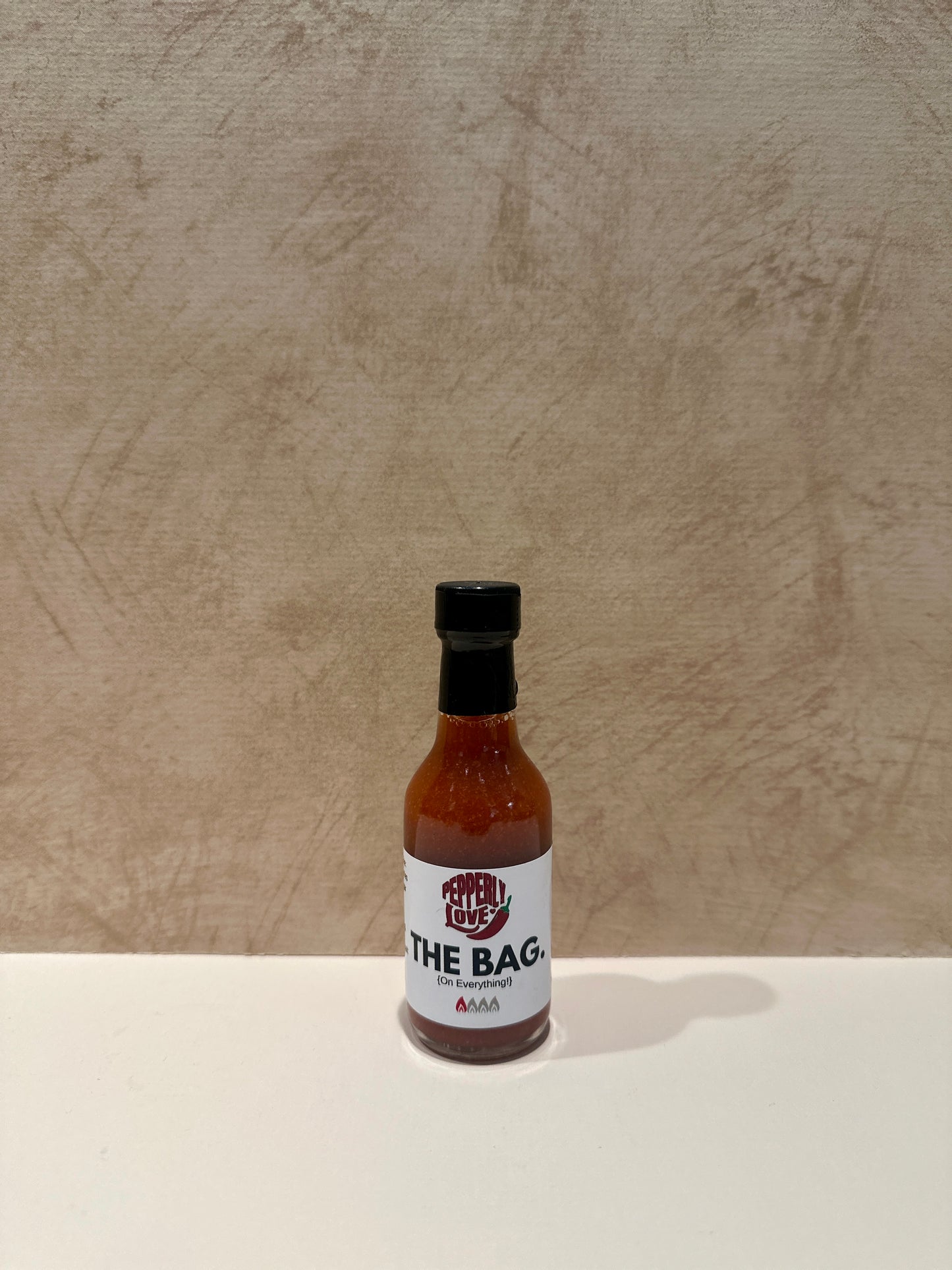 Pepperly Love small The Bag Hot Sauce bottle with a tan background