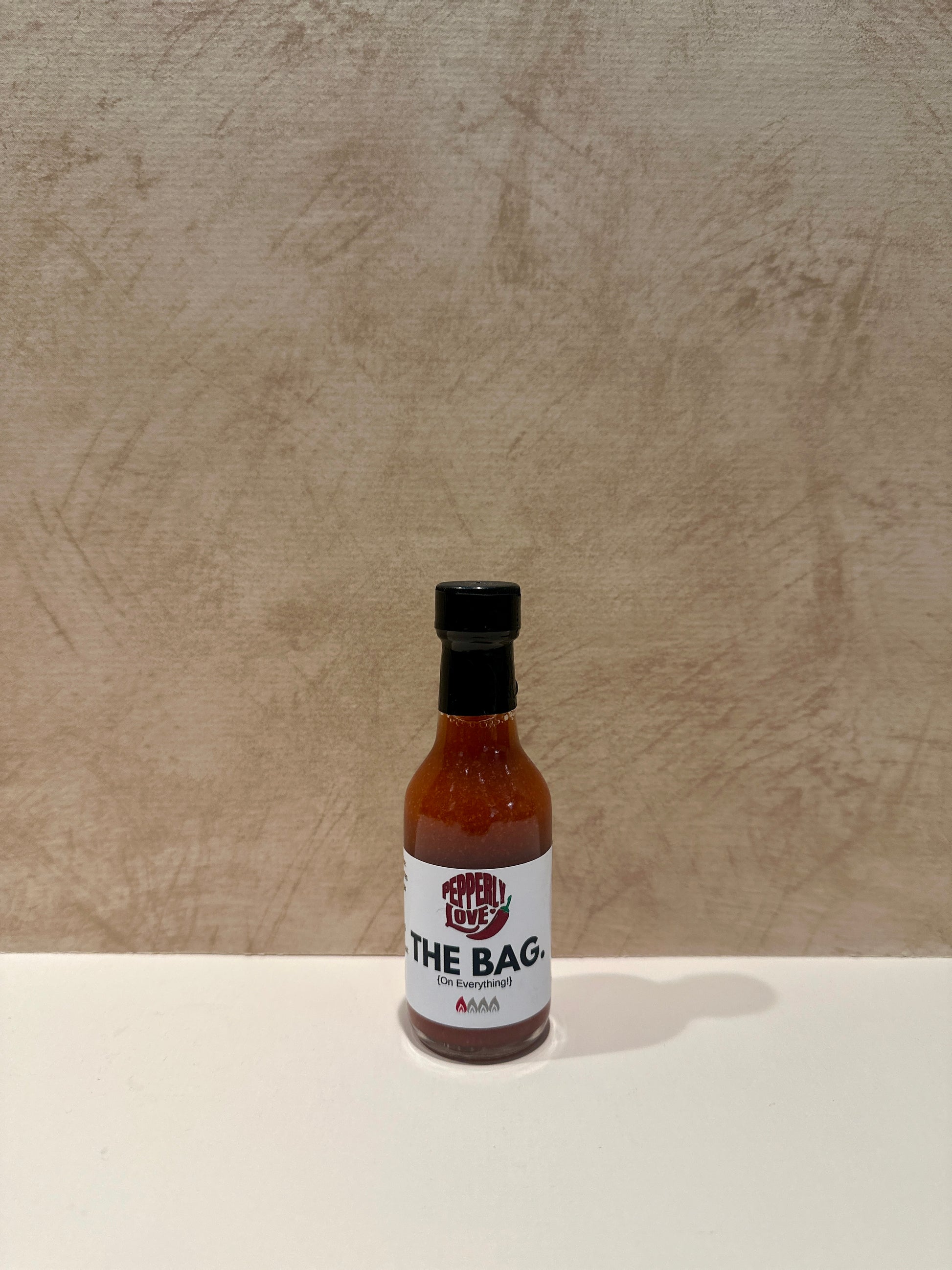 Pepperly Love small The Bag Hot Sauce bottle with a tan background
