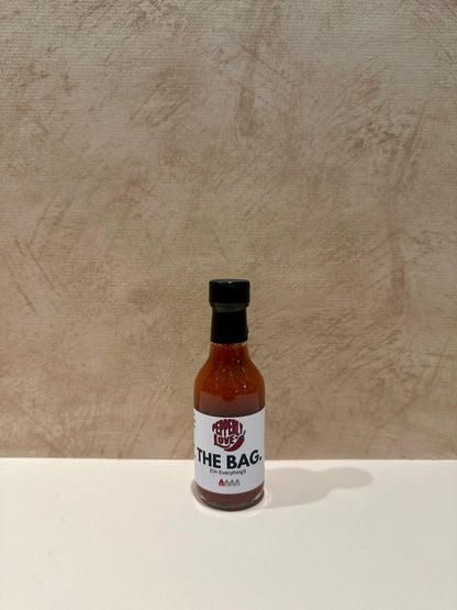 Pepperly Love small The Bag Hot Sauce bottle with a tan background