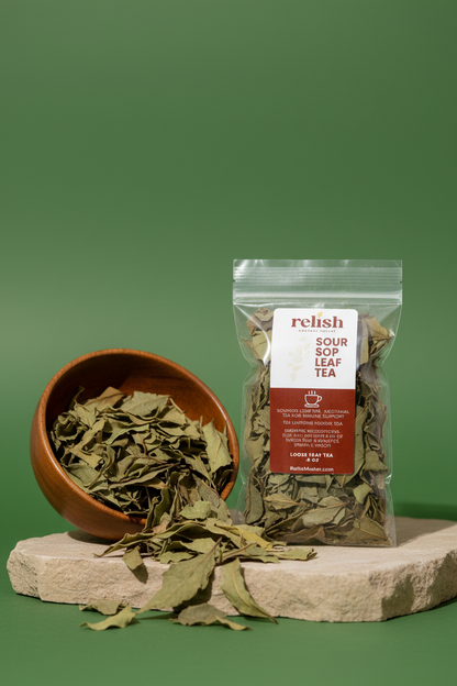 A clear stand-up pouch of Relish Market Soursop Leaf Tea stands on a stone slab next to a wooden bowl filled with dried green soursop leaves, against a solid green background.