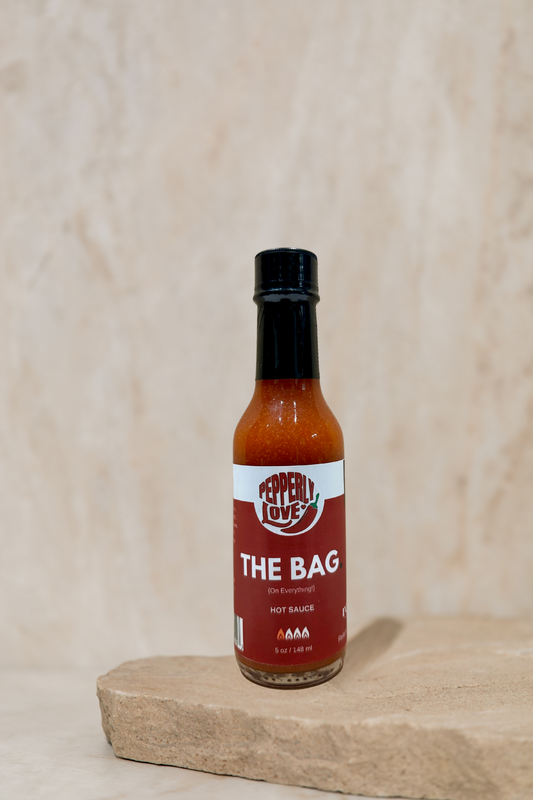 Pepperly Love Large The Bag Hot Sauce jar sitting on a rock slab